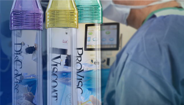 Primer plano de los tres dispositivos viscoquirúrgicos oftálmicos de Alcon. El tubo con tapa morada tiene la marca DisCoVisc, el tubo con tapa amarilla tiene la marca VISCOAT, y el tubo con la tapa verde tiene la marca PROVISC. Detrás de los tubos hay un cirujano con una mascarilla y bata quirúrgica.
