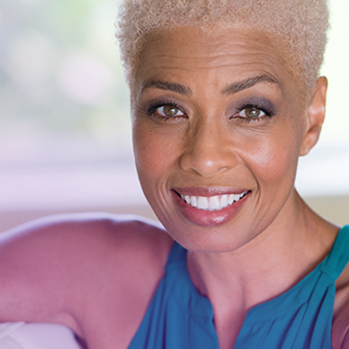 Portrait of a smiling woman with short, platinum blonde hair and warm brown eyes. She is wearing a turquoise top and appears relaxed and confident. 