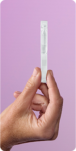 Hand holding a single-dose vial of TRYPTYR eye drops against a light purple background.
